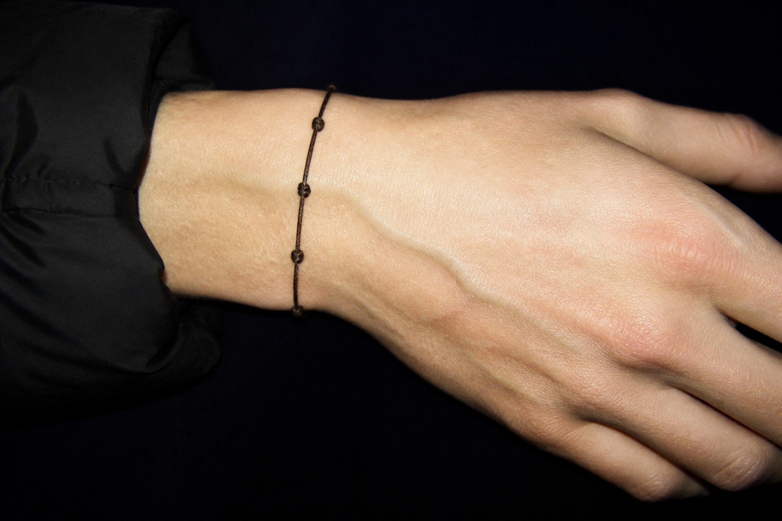 Muñeca con una pulsera fina de metal sobre fondo oscuro