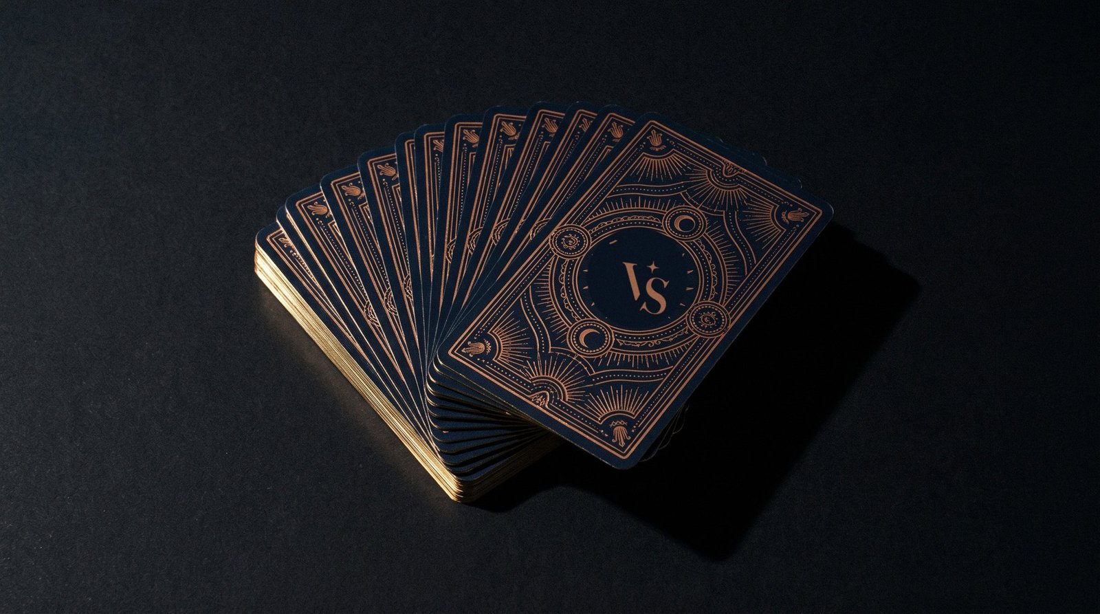 Baraja de tarot de Vibra Santa abierta en abanico sobre una superficie negra, con el sello VS en bronce y luz de flash